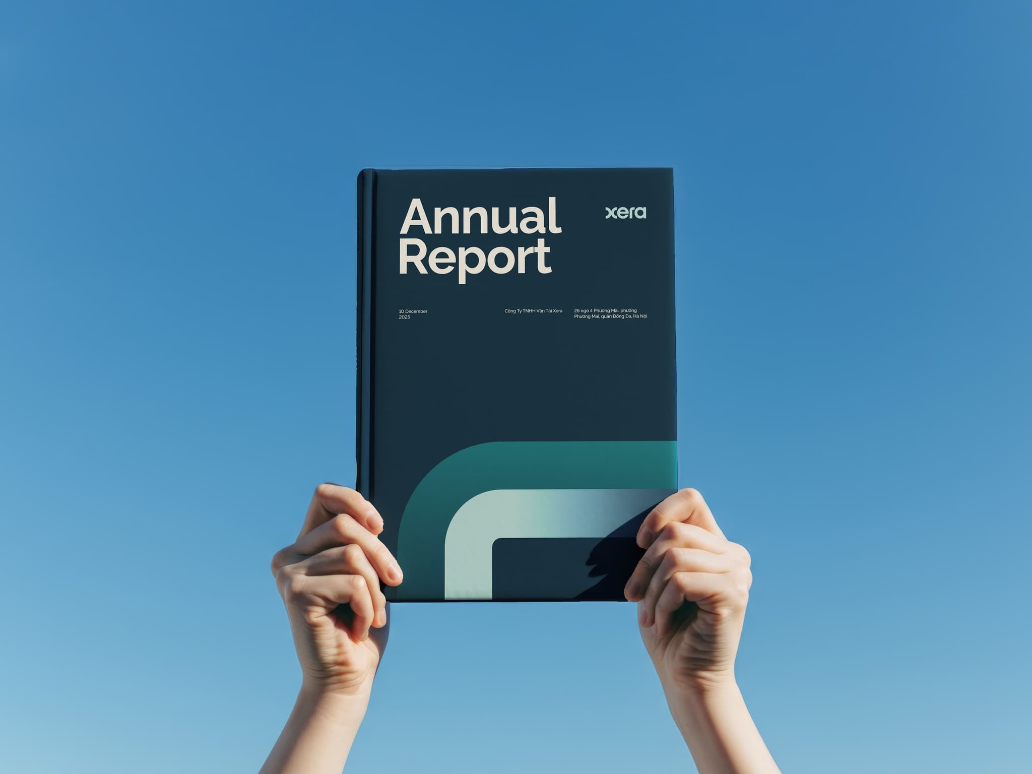 Hands holding an annual report against a clear blue sky, showcasing a modern design.