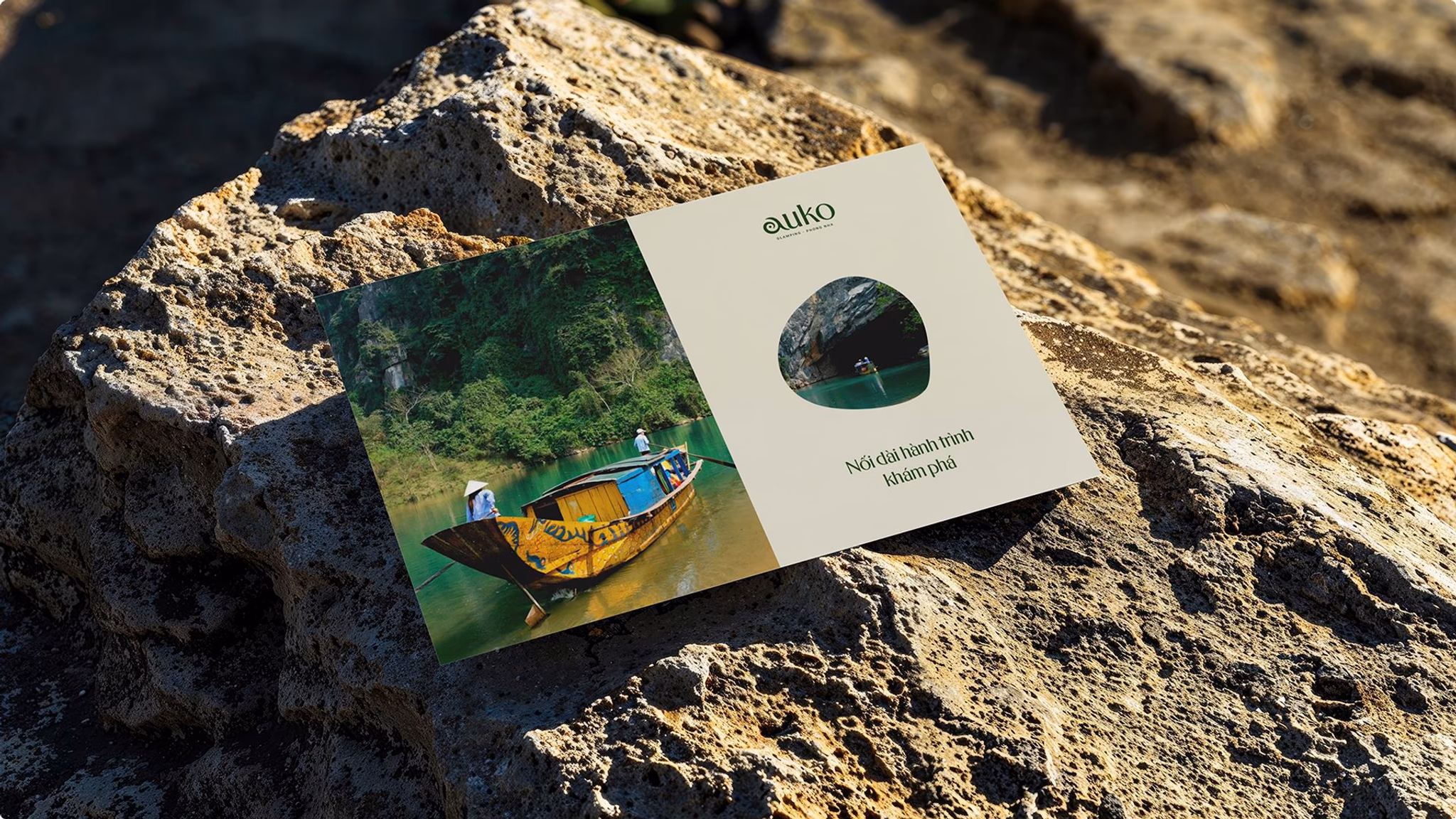 Auko booklet resting on a rock, featuring a colorful boat on a serene water background.