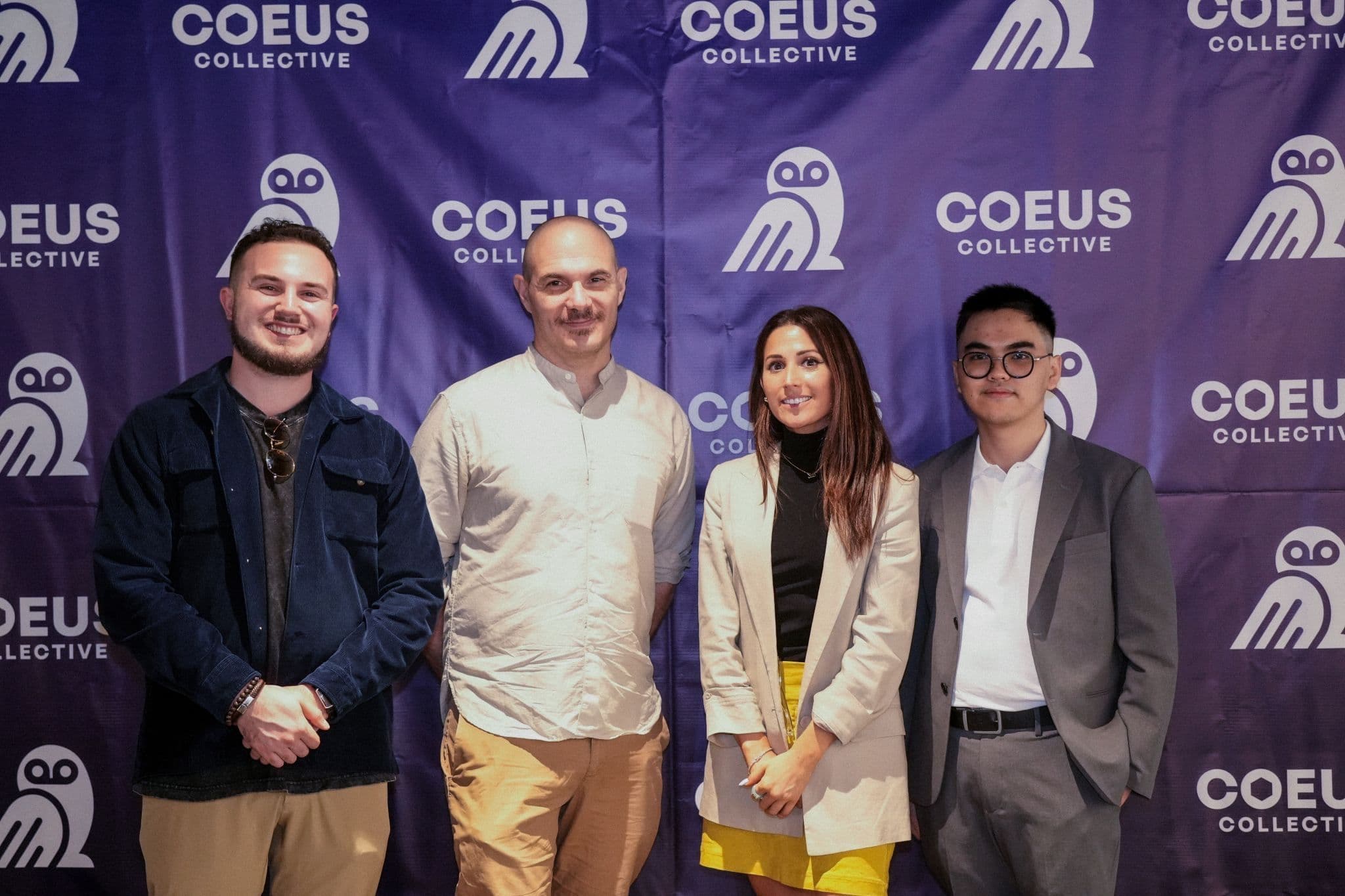 Group of four professionals posing at a Coeus Collective event backdrop, smiling and dressed in business attire.