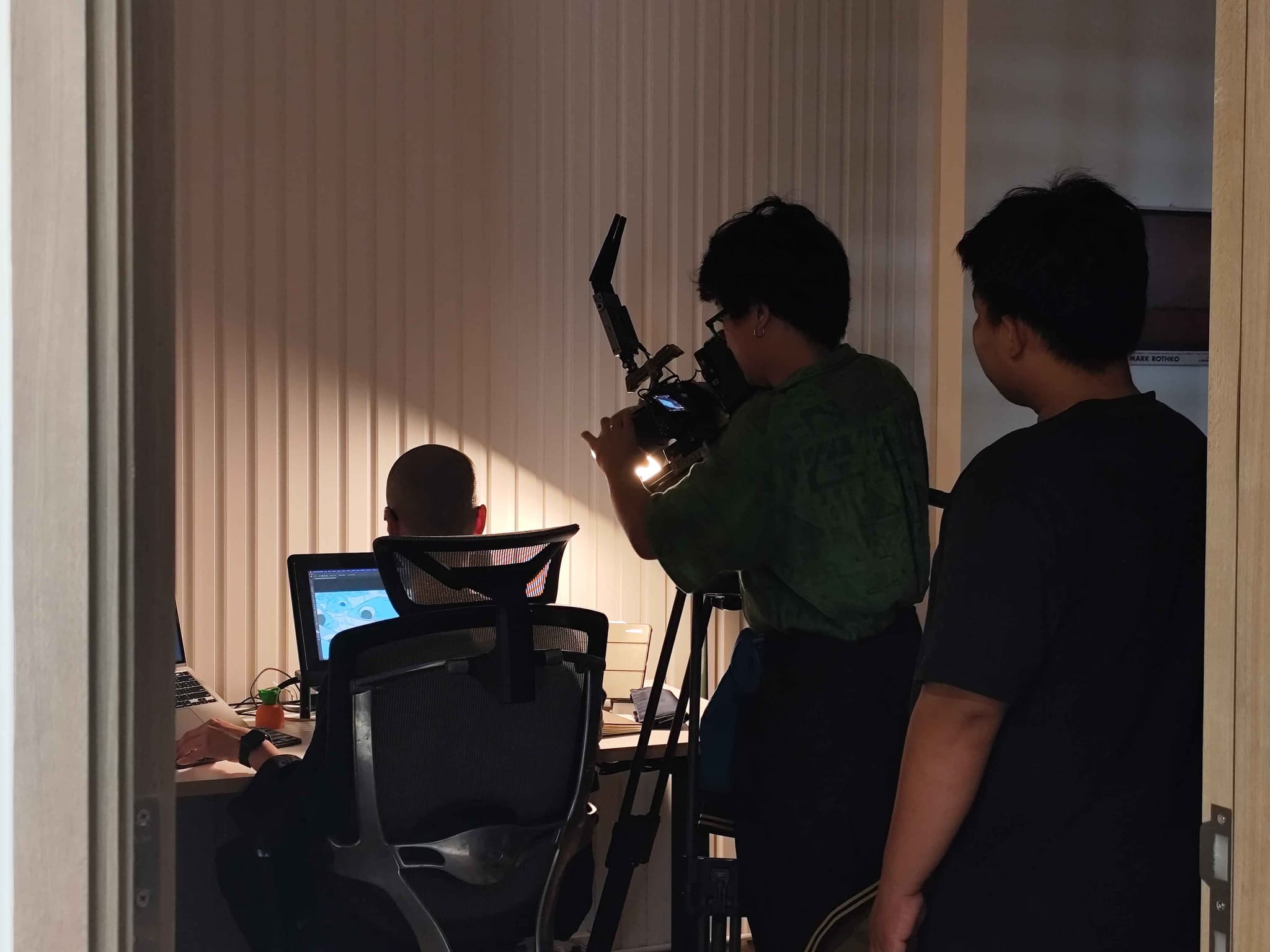Camera crew filming interview in studio room with lighting, microphones, and monitors for video production