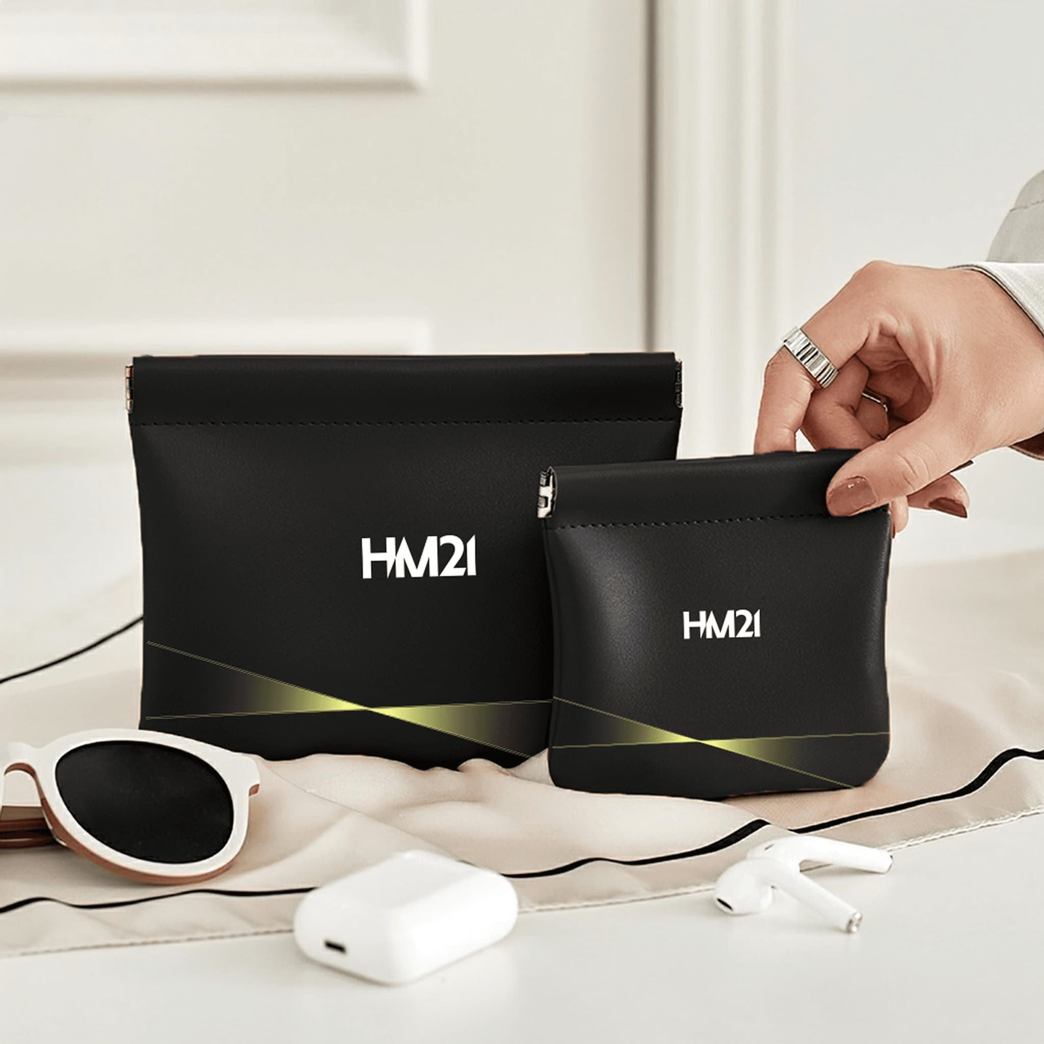 Stylish black HM21 pouches displayed beside sunglasses and earphones on a modern surface.