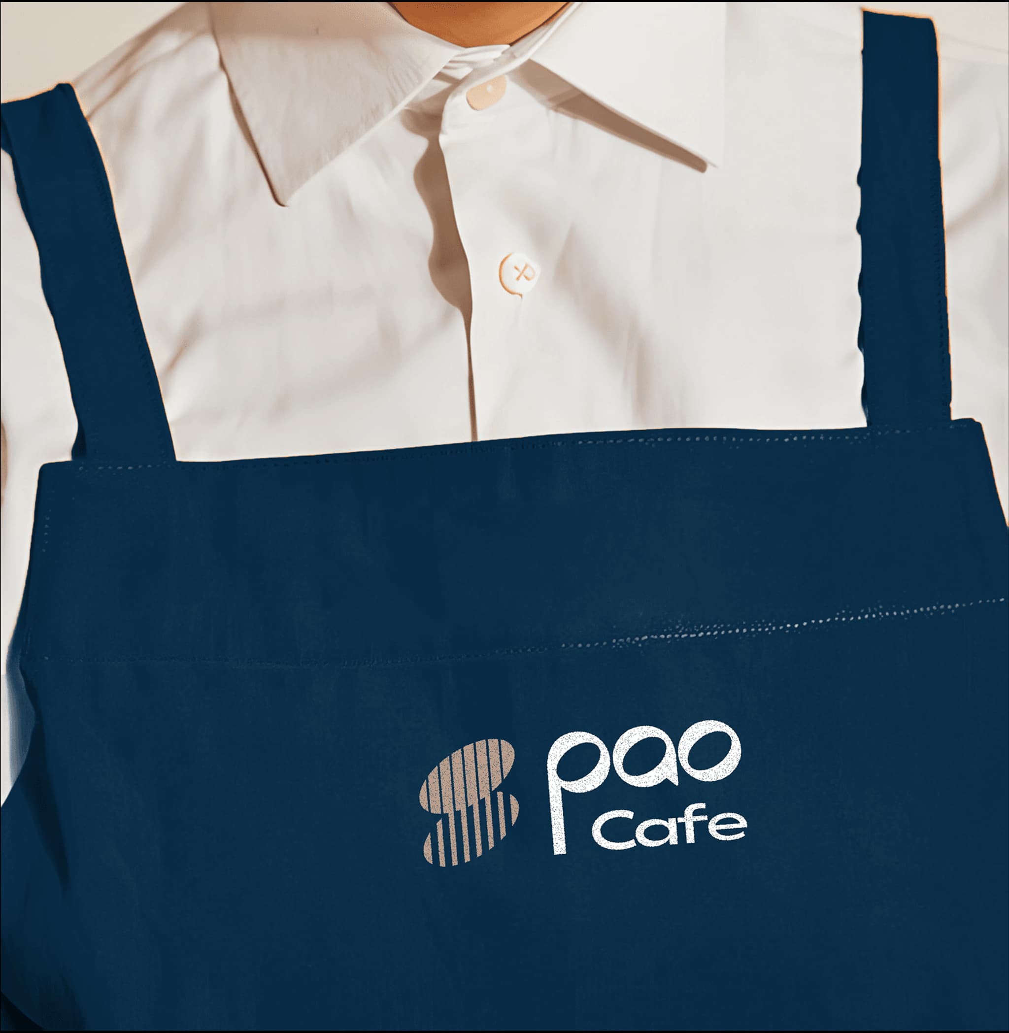 Navy blue apron featuring the "Pao Cafe" logo, worn over a white shirt.