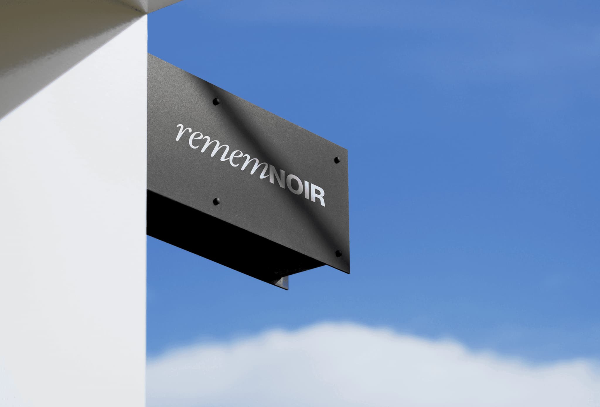 Elegant black and silver logo signage for "remenoir" against a clear blue sky. Ideal for branding and design showcases.