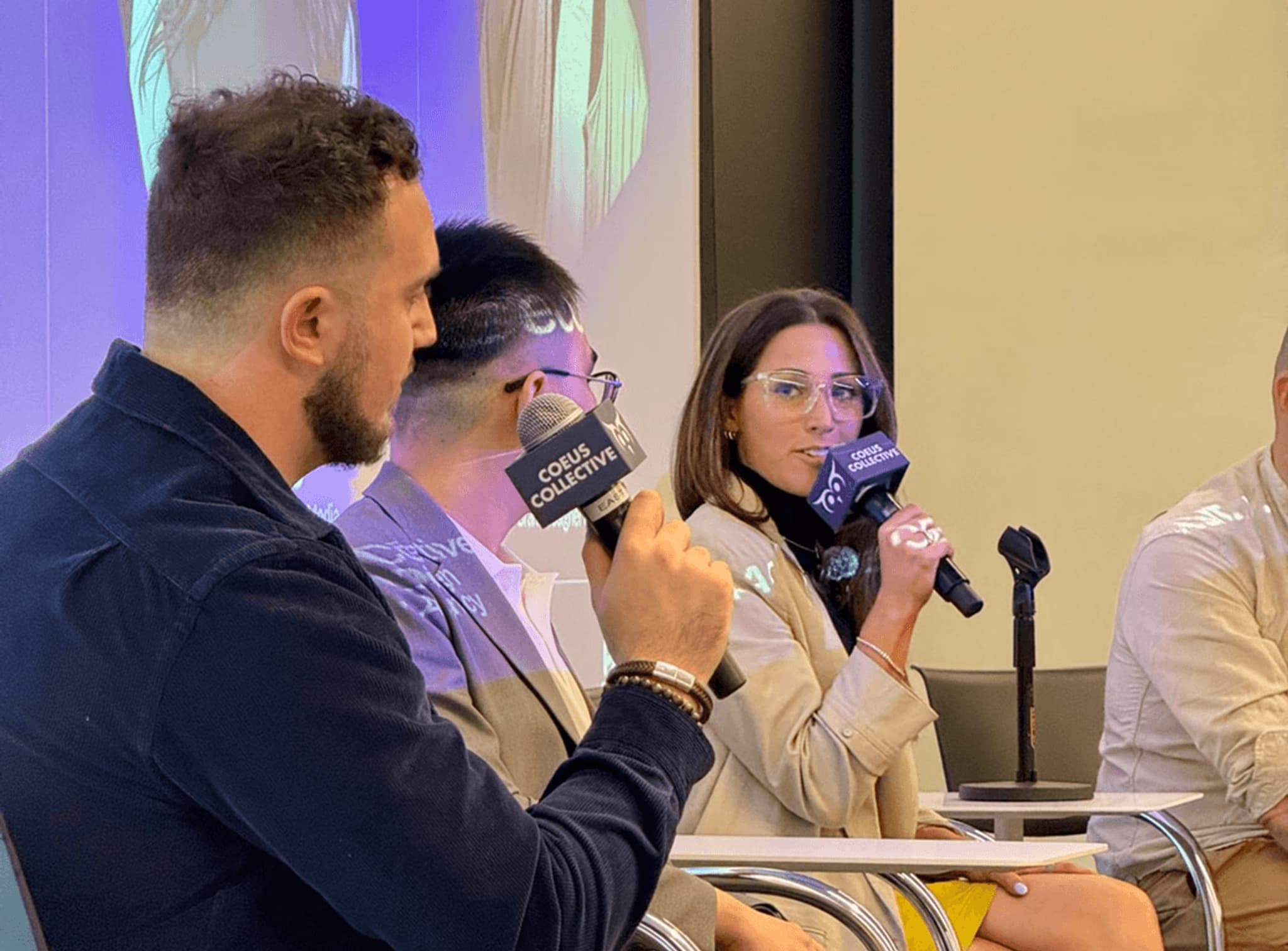 Panel discussion featuring a woman with glasses speaking into a microphone, seated alongside three others at an event.
