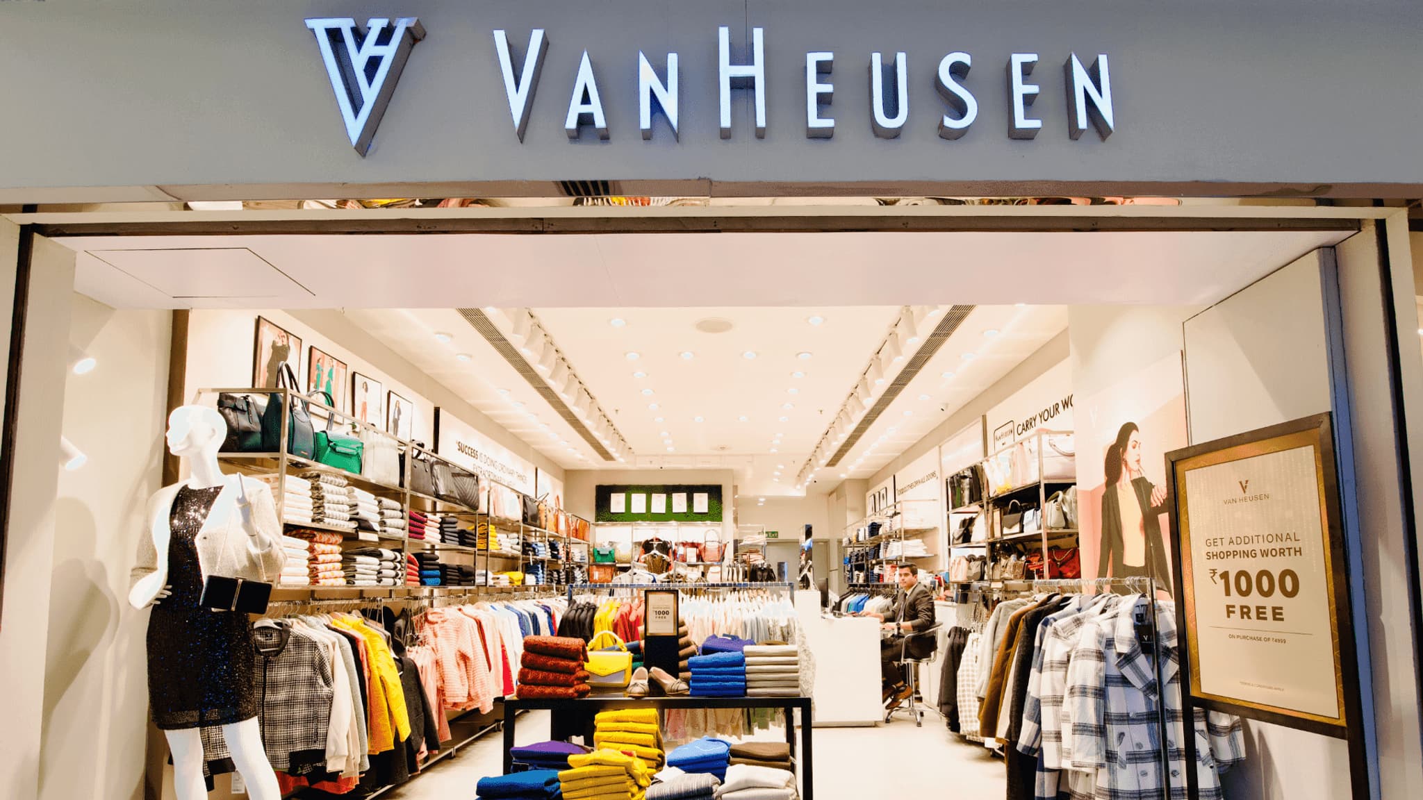 Van Heusen store front showcasing a variety of clothing with a modern interior design and promotional display.
